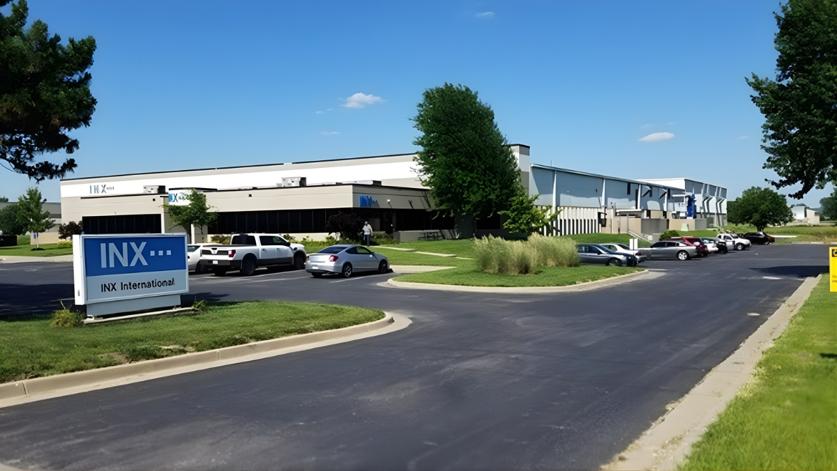 Exterior view of INX International facility with company sign and parked cars.